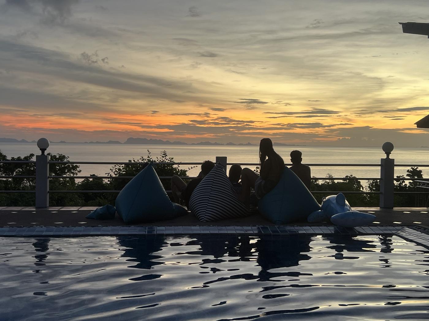 Guests on beanbags by the pool watching the sunset over the islands